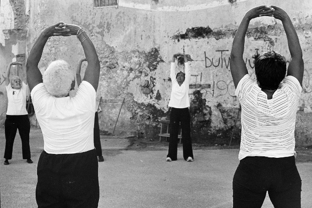 Black and white image of older women standing with their backs to the camera, stretching their arms overhead.